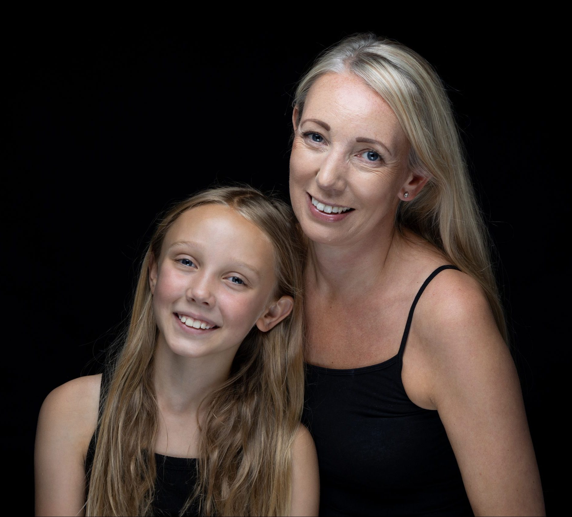 Mother and daughter smiling in black clothing against a black background